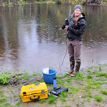 person standing along riverbank with equipment