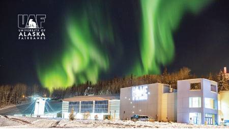 The aurora lights up the winter night sky over the UAF Student Recreation Complex, with the UAF logo in the upper left corner.